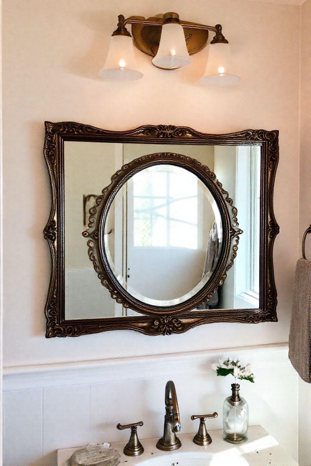 A bathroom features a stylish mirror with an ornate frame, adding elegance and visual interest to the space. The mirror is strategically placed above the vanity, creating a focal point and complementing the existing bathroom decor. Soft, natural light illuminates the room, highlighting the mirror's intricate details and reflective surface. The overall aesthetic is elegant, sophisticated, and inviting.